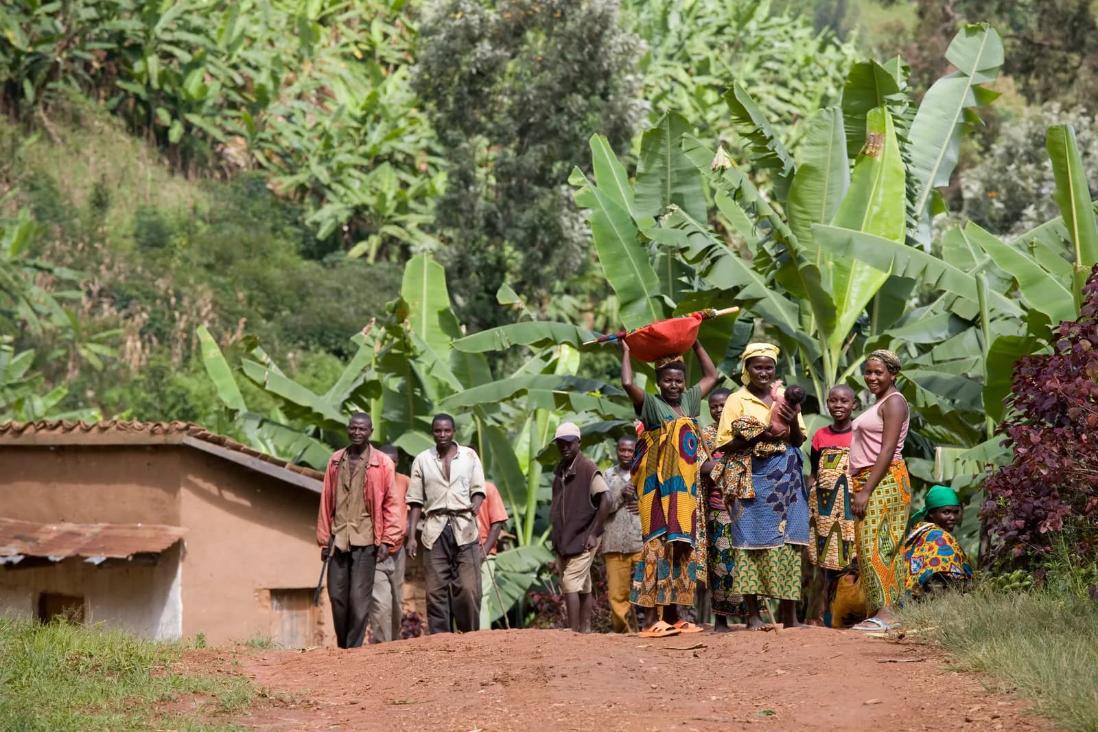 People gathered beside a rural home surrounded by banana plants